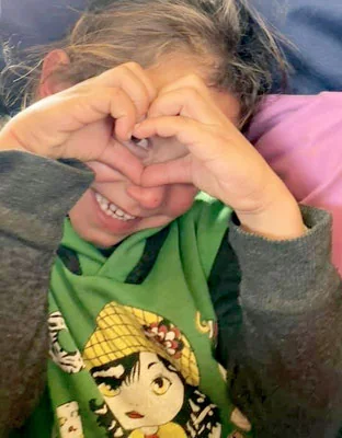 A young girl makes a heart with her hands
